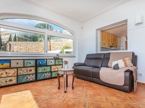 A living room with a sofa, a small table, a decorative cabinet, and large windows.