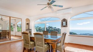 A dining area with a table and chairs, large windows, a ceiling fan, and a stone wall. - Wonderful private villa for 10 people with private pool, WIFI, TV and pets allowed (Lloret De Mar)