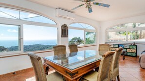 A dining area with a glass-top table, wicker chairs, and a ceiling fan. - Wonderful private villa for 10 people with private pool, WIFI, TV and pets allowed (Lloret De Mar)