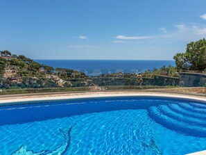 Ein klares, blaues Schwimmbecken mit Blick auf das Meer und eine Hügelkuppe.