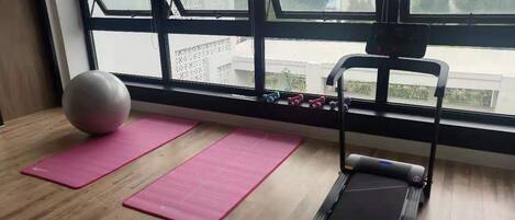 Un gimnasio con cinta de correr, colchonetas rosas y pelotas de ejercicio.