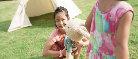 A tent and two children playing with stuffed animals in a grassy area.