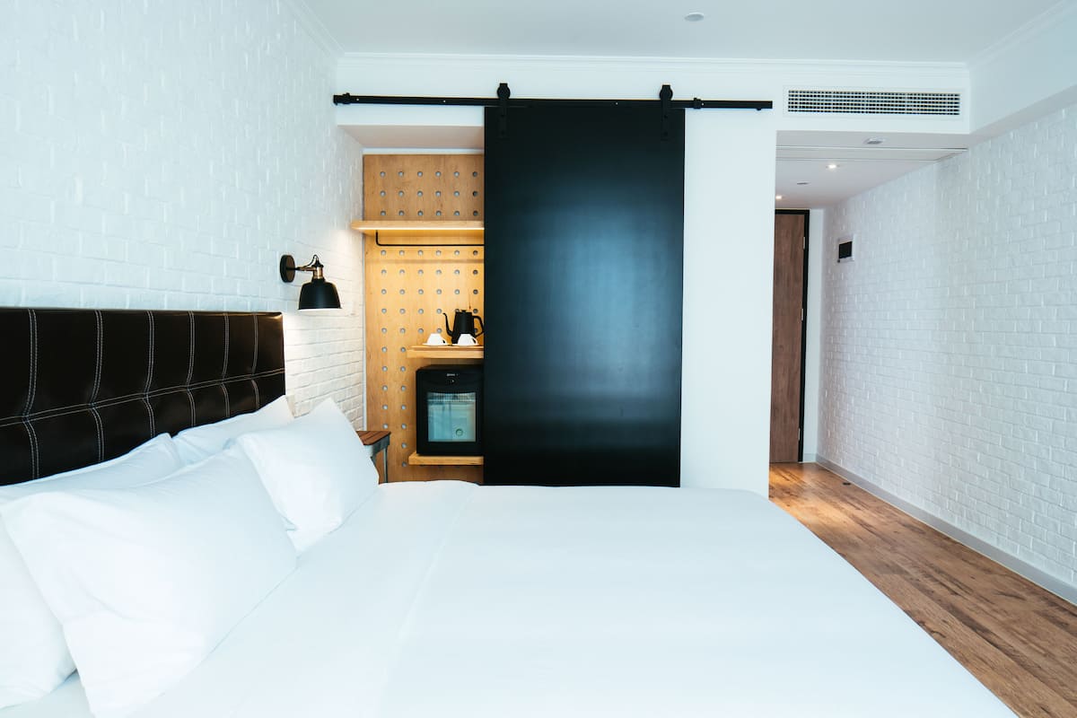 Una habitación de hotel moderna con una cama grande, un cabecero de madera, una puerta corrediza negra y una pequeña zona de kitchenette.