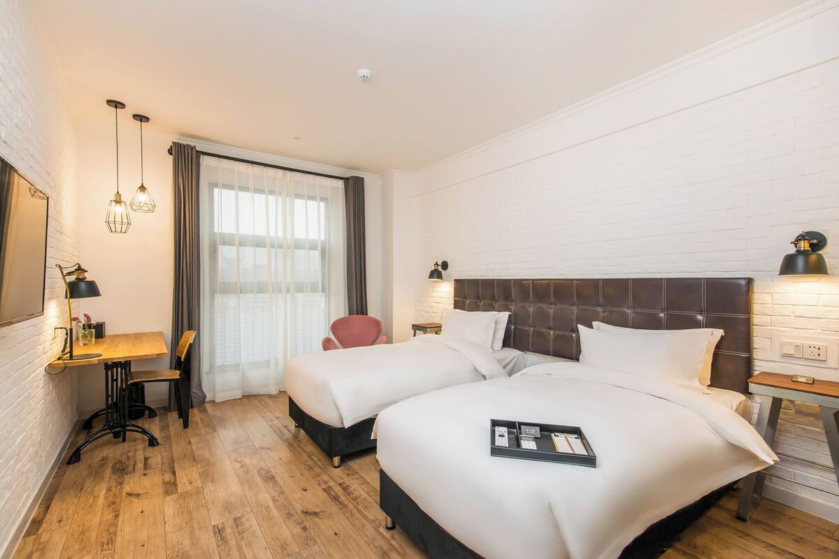 Habitación de hotel con dos camas, un escritorio, una silla, un televisor y una ventana con cortinas.