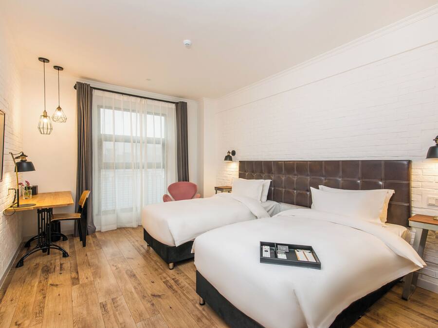 A hotel room with two beds, a desk, a chair, a TV, and a window with curtains.