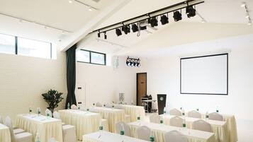 Una sala de conferències amb taules, cadires, una pantalla de projector i un escenari amb il·luminació.