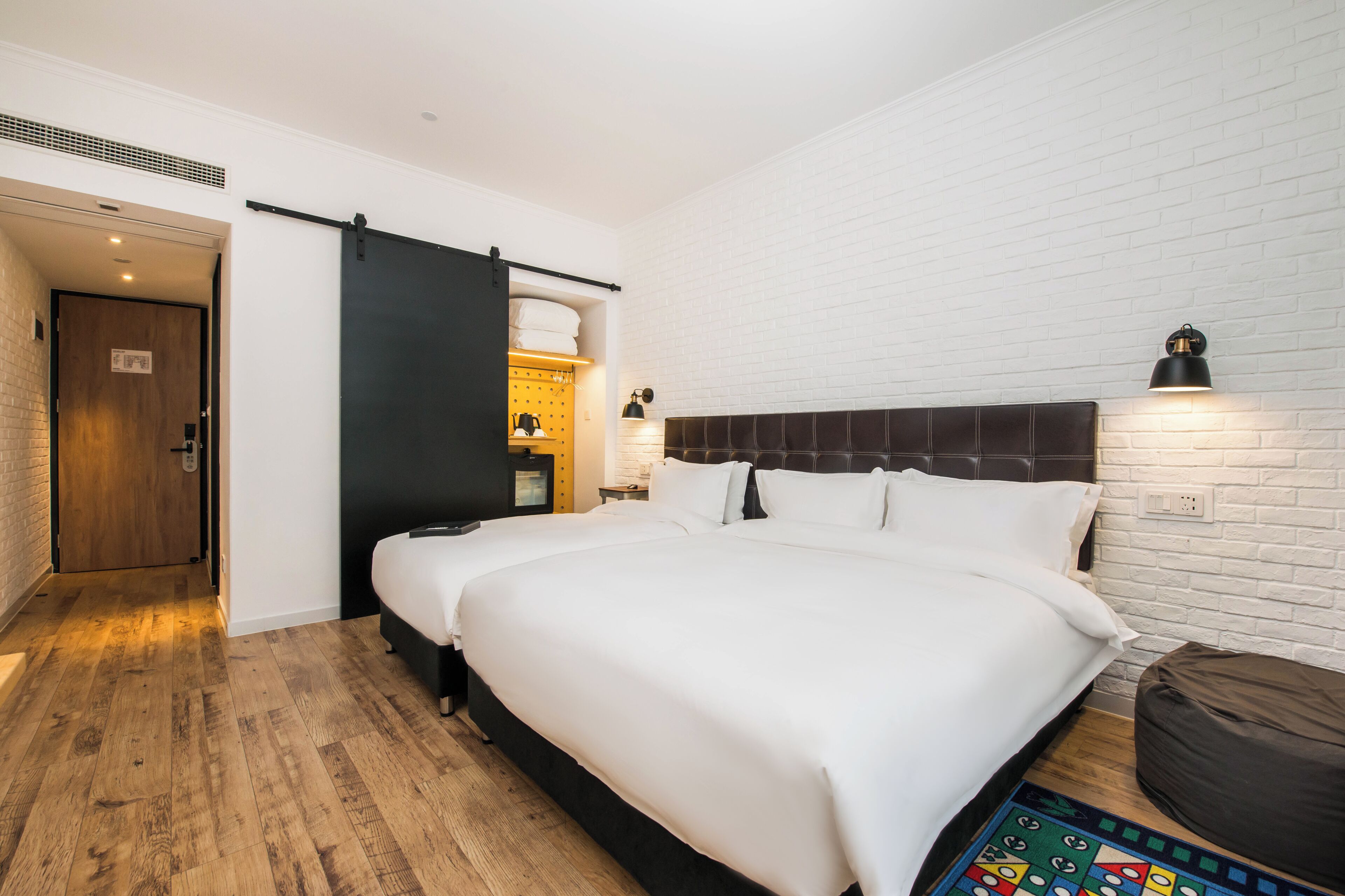 Une chambre d’hôtel avec un grand lit, une armoire à portes coulissantes, une petite table avec une lampe et un mur en briques.