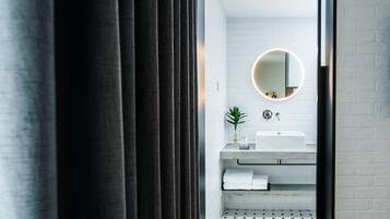 A modern bathroom with a white tiled wall, a round mirror, a sink, and a potted plant.