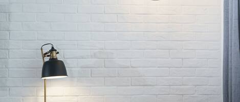 Una mesa de madera con una lámpara negra, una silla y dos lámparas colgantes frente a una pared de ladrillo blanco.