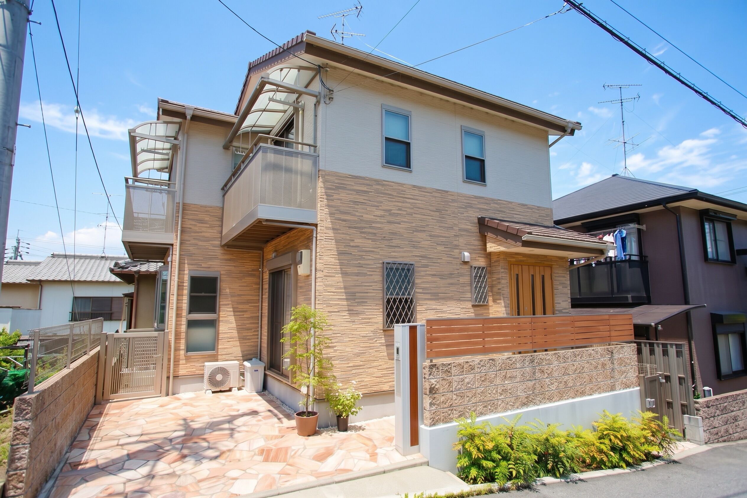 A two-story residential building with a balcony, a small garden, and a tiled patio area.