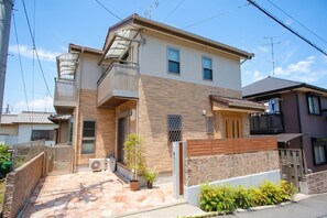 A two-story residential building with a balcony, a small garden, and a tiled patio area.