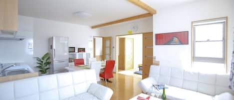A modern living room with white sofas, a dining area, and a kitchen.