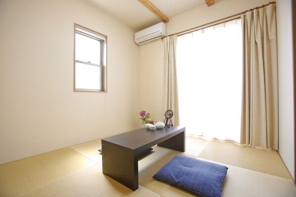 A room with tatami flooring, a low table, a window with a curtain, and an air conditioning unit.