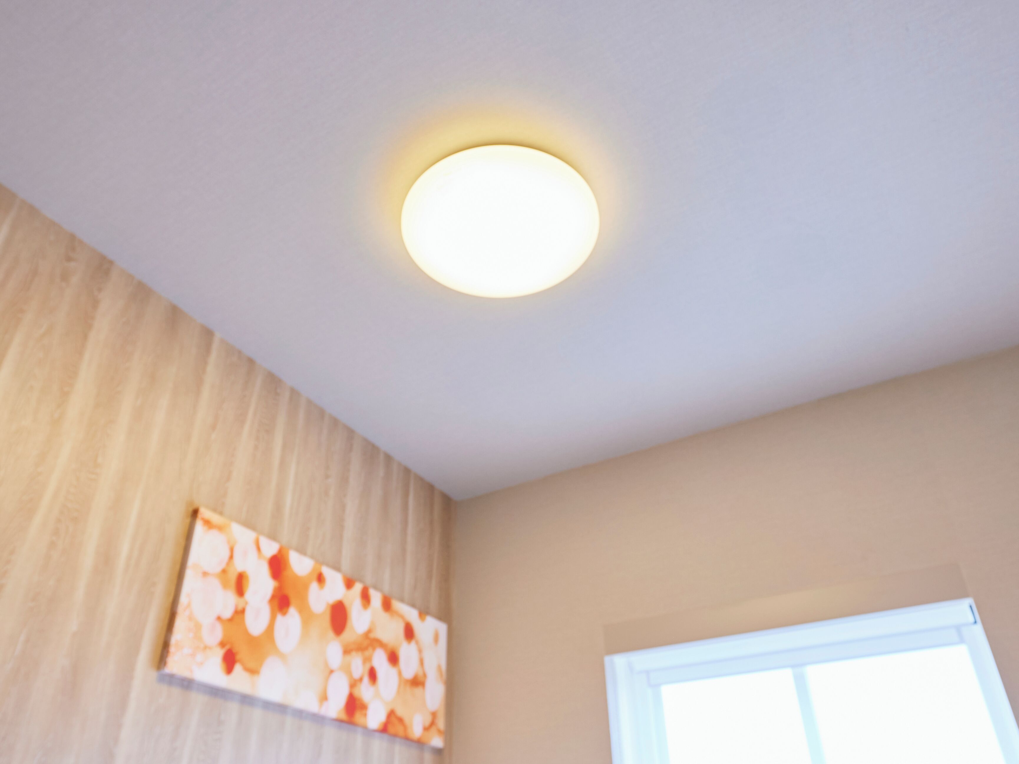 A room with a ceiling light, a window, and a wall with a patterned design.