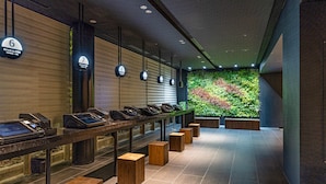 A modern hotel lobby with a long reception desk, numbered signs, and a green wall with plants. - Ours Inn Hankyu (Tokyo)