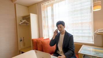 A hotel room with a bed, a desk, a telephone, and a window with blinds.
