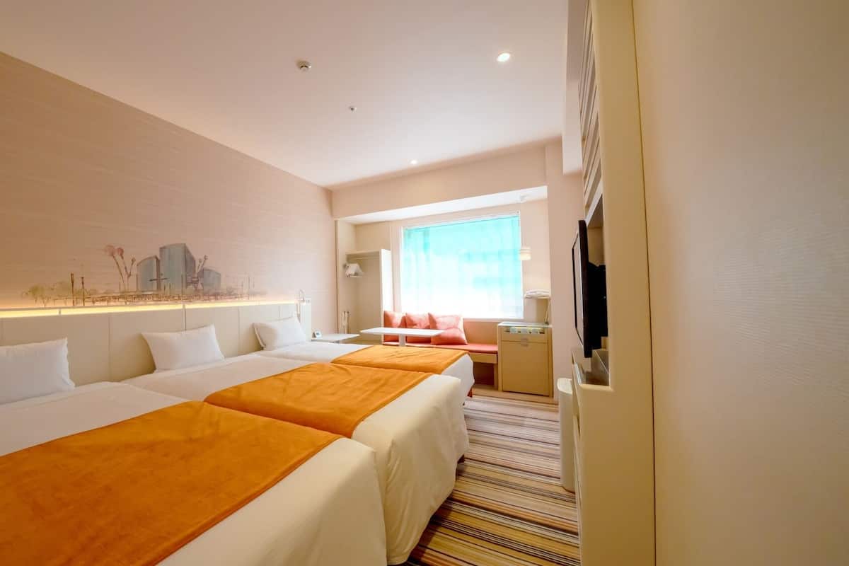 A hotel room with two beds, a TV, a desk, and a window with curtains.
