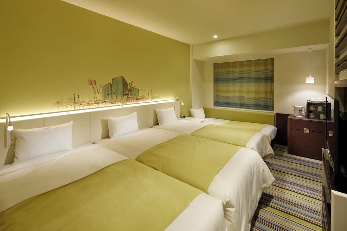 A hotel room with two beds, a desk, a coffee maker, and a painting on the wall.