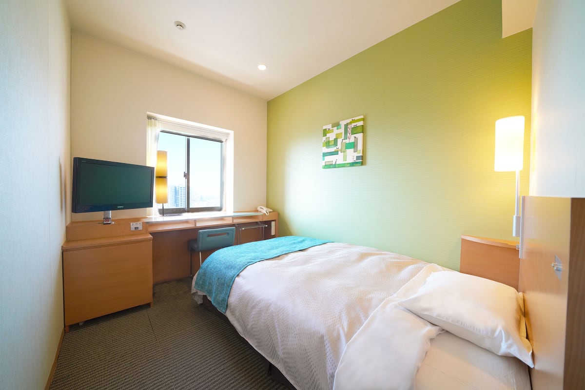 A hotel room with a bed, desk, chair, and a television.