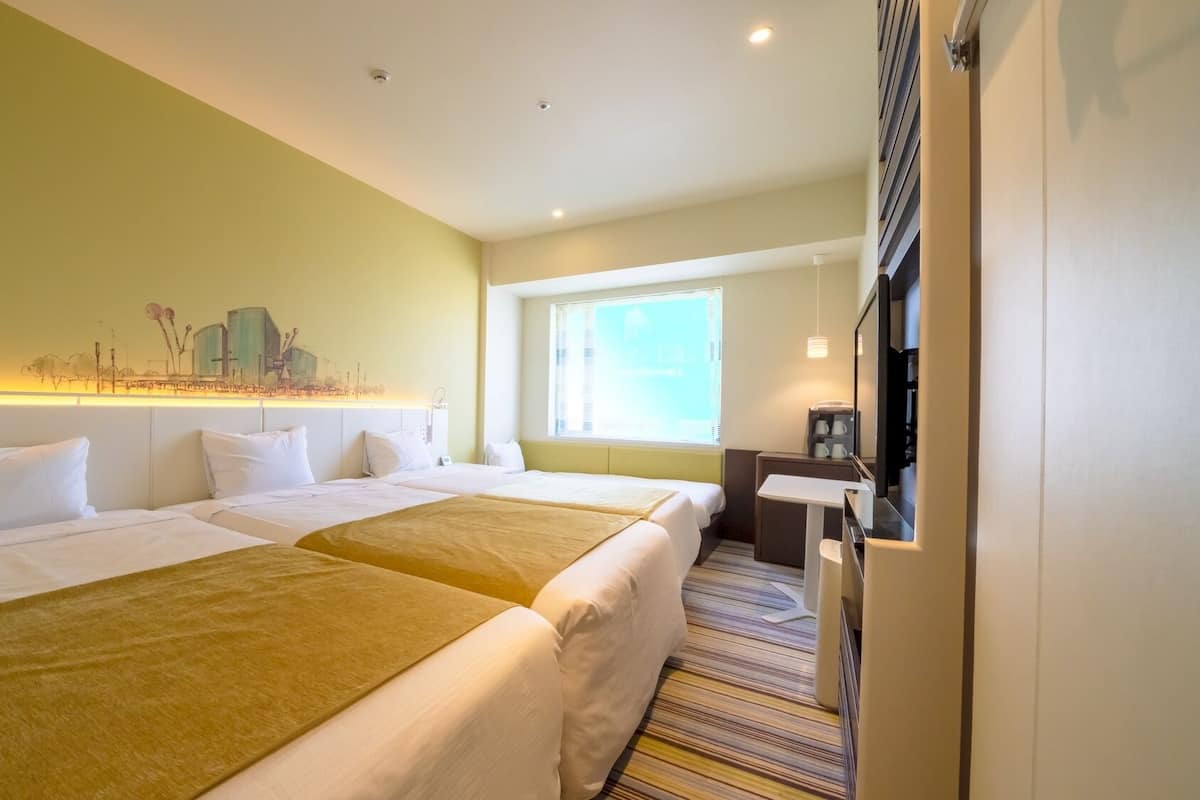 A hotel room with two beds, a desk, a chair, a window with blinds, and a wall-mounted artwork.