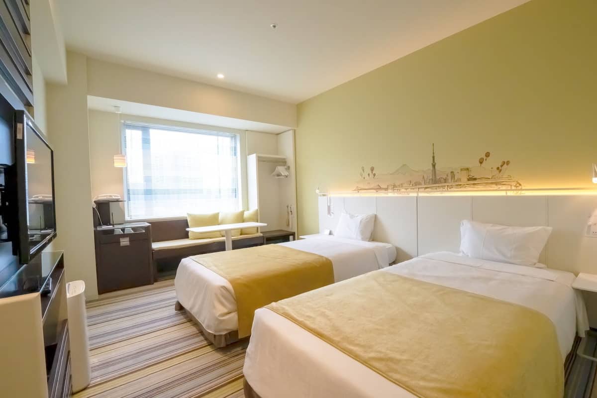 A hotel room with two beds, a desk, a television, and a window with blinds.