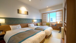 A hotel room with two beds, a desk, a chair, a window with a city view, and a bedside table with a lamp. - Ours Inn Hankyu (Tokyo)