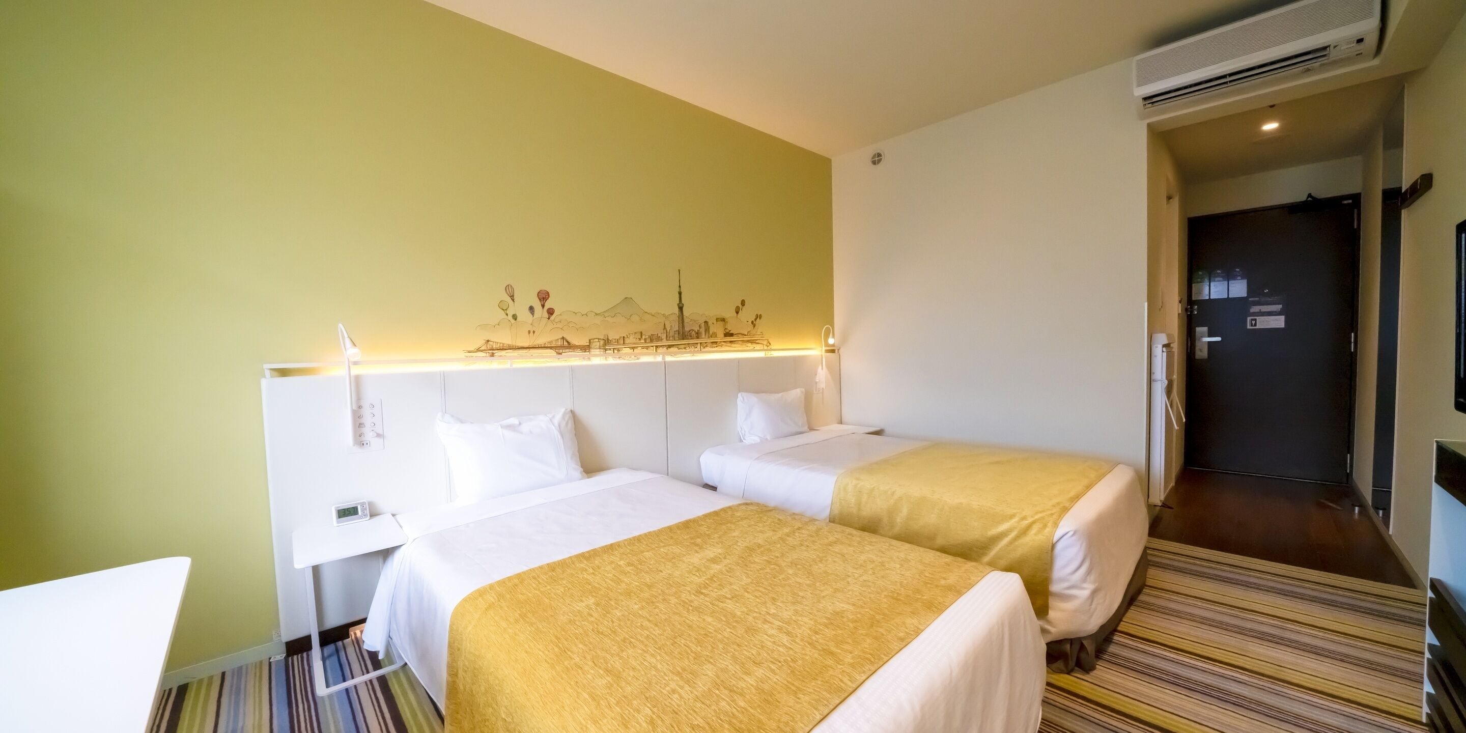 Ein Hotelzimmer mit zwei Betten, einem Schreibtisch, Wandbild und einer Tür.