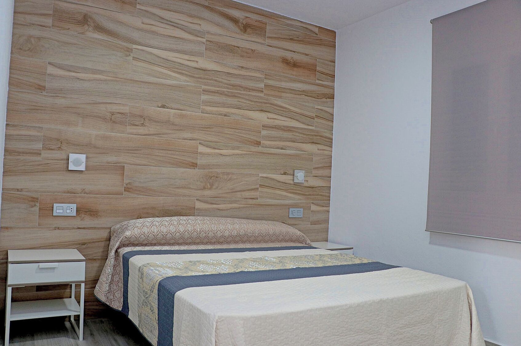 Un dormitorio con dos camas, una mesita de noche blanca y un panel de pared de madera.