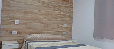 Un dormitorio con dos camas, una mesita de noche blanca y un panel de pared de madera.
