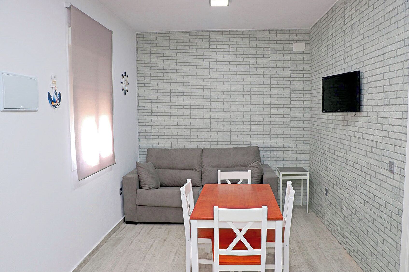 Ein gemütlicher Wohnbereich mit einer Couch, einem Esstisch und einem an einer Ziegelwand befestigten Fernseher.