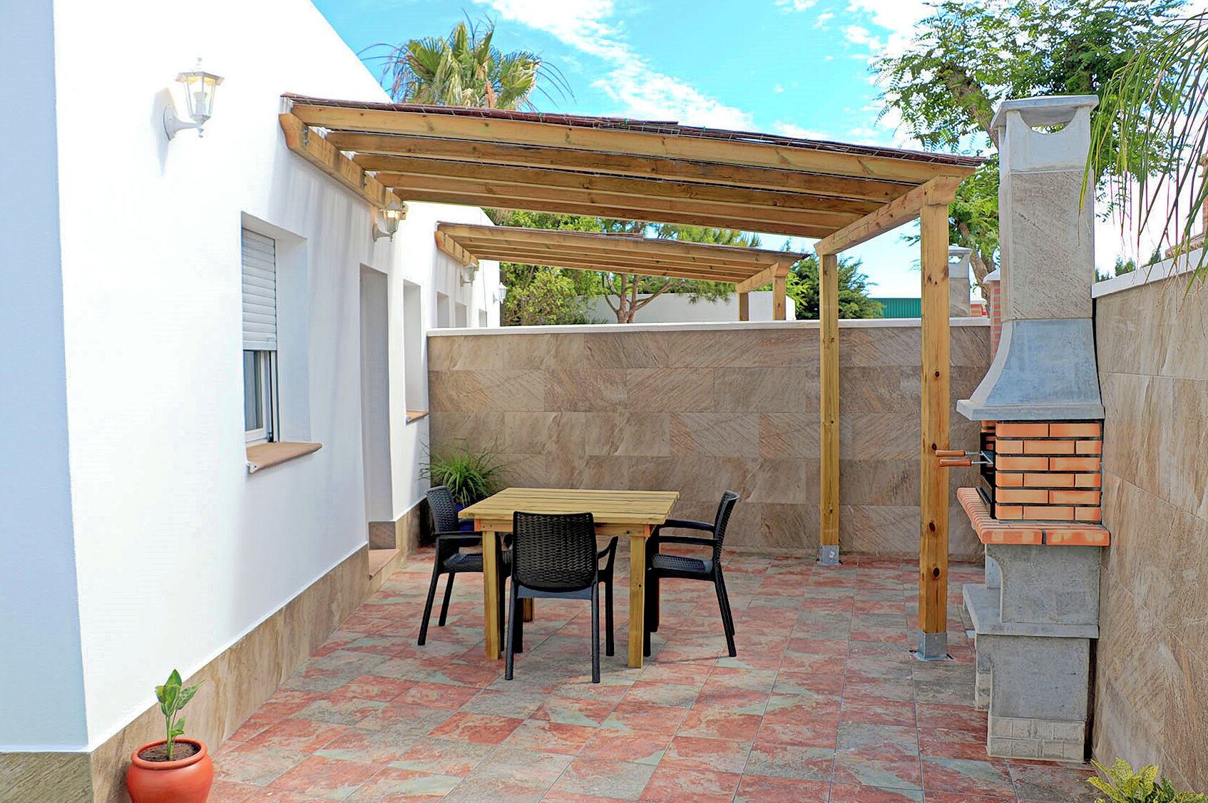 Een terras met een houten pergola, een bakstenen barbecue en een betegelde vloer.