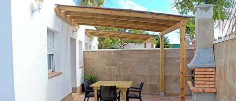 Een terras met een houten pergola, een bakstenen barbecue en een betegelde vloer.