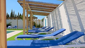 A row of blue and white sun loungers under a wooden pergola, with a pool and greenery in the background. - Bungalow with Wi-Fi and shared pool (CONIL DE LA FRONTERA)