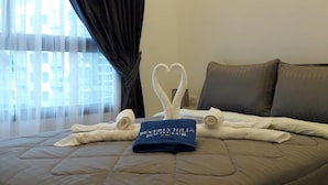 Ett hotellrum med en stor säng, mörka gardiner, en blå handduk med text på och en hjärtformad dekoration av handdukar.