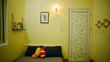 Quarto com cama, almofadas, luminária na parede, porta com padrão floral e uma prateleira pequena com um sinal de Wi-Fi.