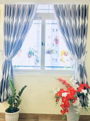 A room with a window covered by curtains, a potted plant, and a vase with flowers. - Quy Nhon Homestay BnB (Quy Nhon)