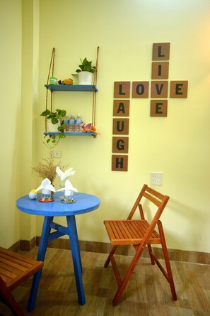 A room with a blue table, a wooden chair, and a shelf with plants and bottles. - Quy Nhon Homestay BnB (Quy Nhon)