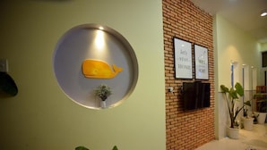 A reception area with a circular wall decoration featuring a whale, a small potted plant, and two framed signs on a brick wall. - Quy Nhon Homestay BnB (Quy Nhon Nam)
