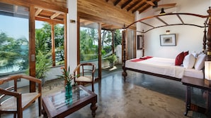 A spacious room with a large bed, wooden furniture, and a view of lush greenery outside. - Royal Indigo Villa (Unawatuna)