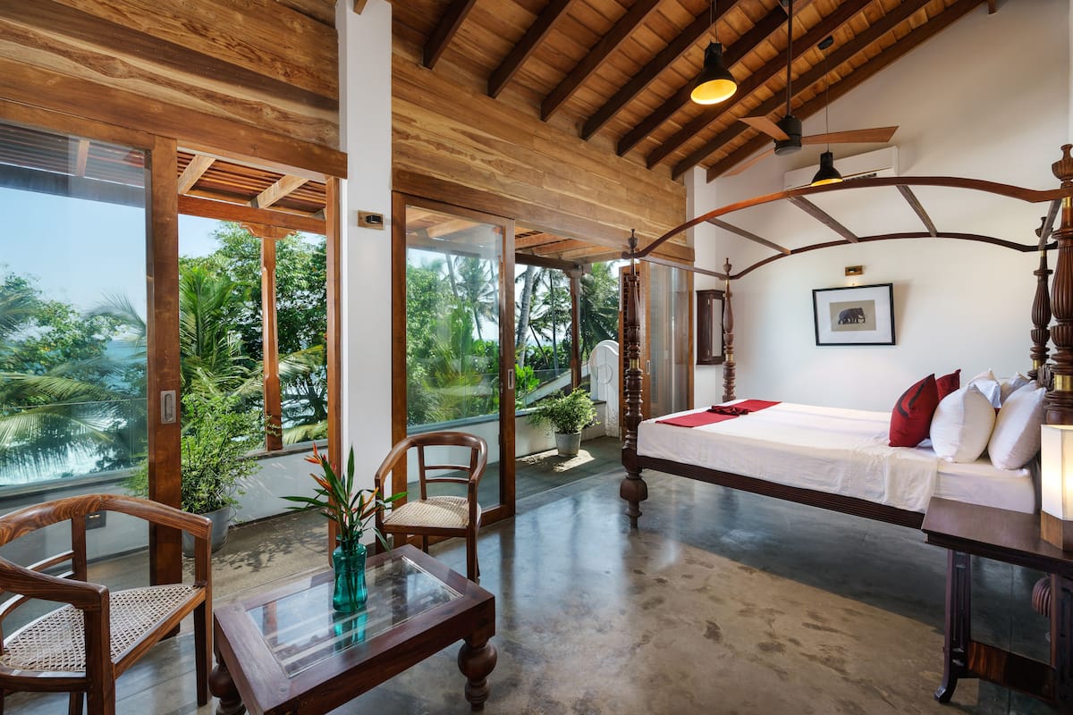 A spacious room with a large bed, wooden furniture, and a view of lush greenery outside.
