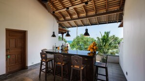 A kitchen with a wooden ceiling, a bar area with stools, a wooden door, and a view of the ocean. - Royal Indigo Villa (Unawatuna)