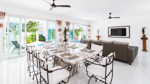 A spacious living area with a large marble dining table, white bar stools, a grey sofa, and a TV mounted on the wall. - Wirason Villa 4 Bedrooms (Koh Samui)