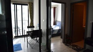 A hotel room with a bed, a desk, a chair, a window with curtains, and a view of the outside building. - The Base Central Pattaya by Arawat (Pattaya)
