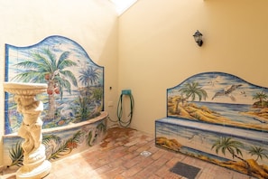 A room with a tiled mural of a tropical scene, a white pedestal, and a bench with a similar mural.