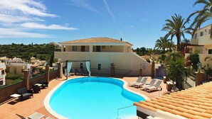 A swimming pool with lounge chairs, a building with a tiled roof, and palm trees.