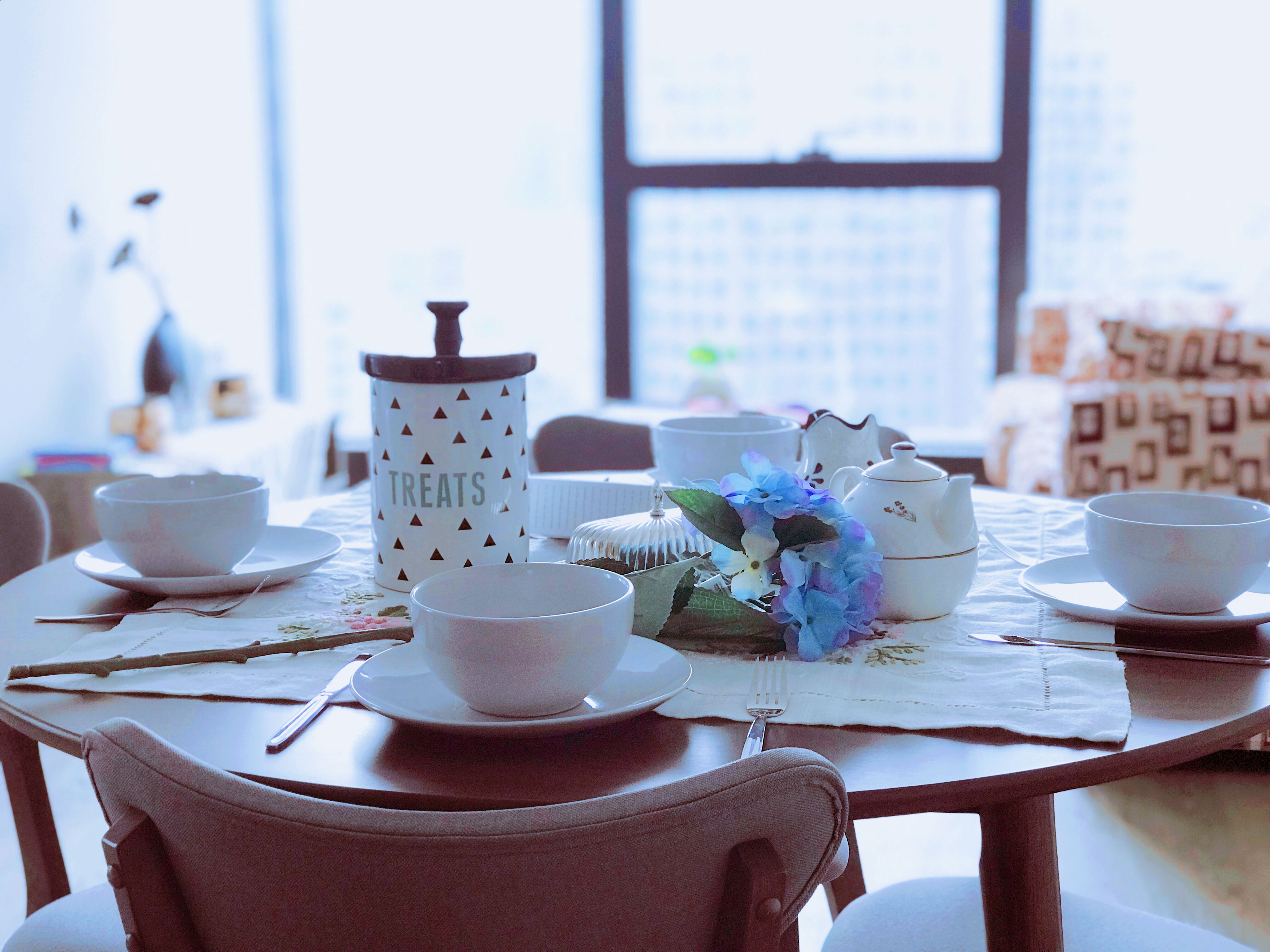 A dining table set with white ceramic tea sets and a decorative vase with blue flowers.