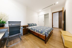 A modern bedroom with a bed, a desk with a chair, a wardrobe, and a small table.