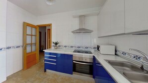 Eine Küche mit weiß gefliesten Wänden, einer blau-weißen Küchenrückwand, einem Einbauofen, einer Mikrowelle und einer Spüle aus Edelstahl.