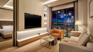 A modern hotel room with a bed, a sofa, a TV, a small table, and a window with a city view. - Shinhwa Jeju Shinhwa World Hotel & Resorts (Seogwipo)