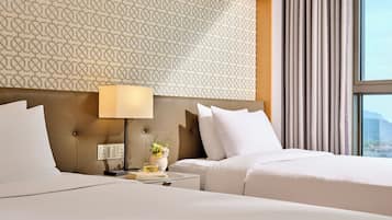A hotel room with two beds, a patterned headboard, a bedside table with a lamp, and a window with curtains.